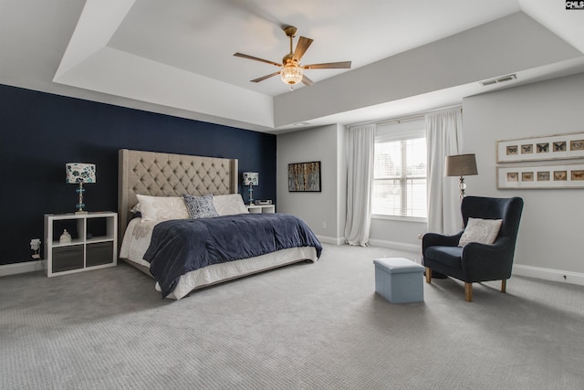 carpeted bedroom featuring a ceiling fan, a tray ceiling, visible vents, and baseboards