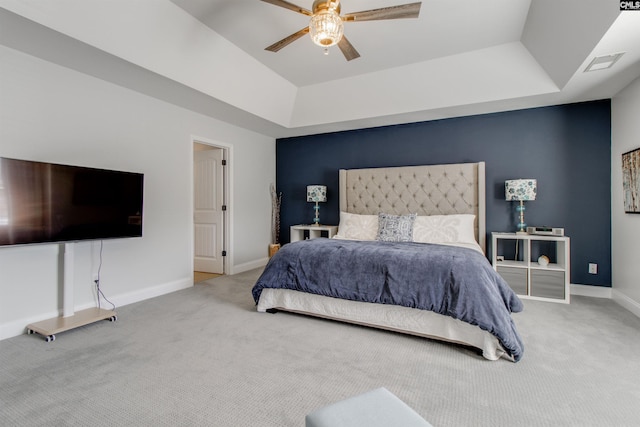 carpeted bedroom featuring a ceiling fan, a tray ceiling, visible vents, and baseboards