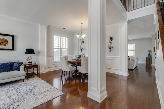 dining room featuring dark wood-type flooring, a decorative wall, ornate columns, and ornamental molding