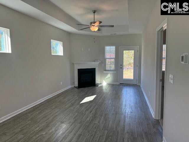 unfurnished living room featuring baseboards, a raised ceiling, a ceiling fan, dark wood finished floors, and a fireplace