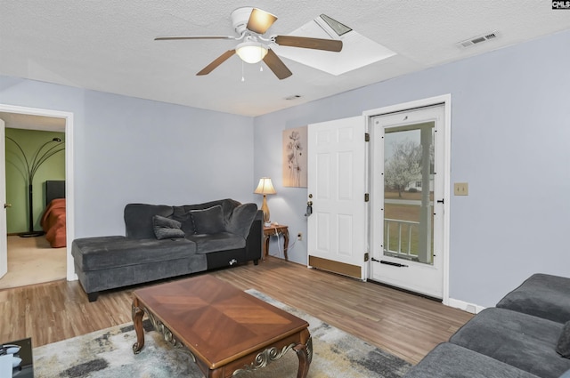 living room featuring a textured ceiling, ceiling fan, wood finished floors, and visible vents