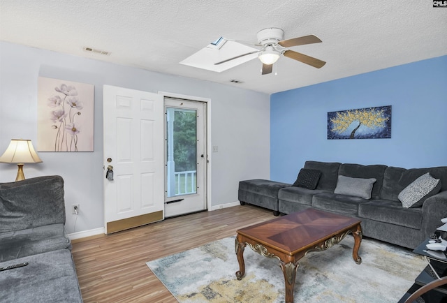 living area featuring a textured ceiling, a skylight, wood finished floors, visible vents, and baseboards