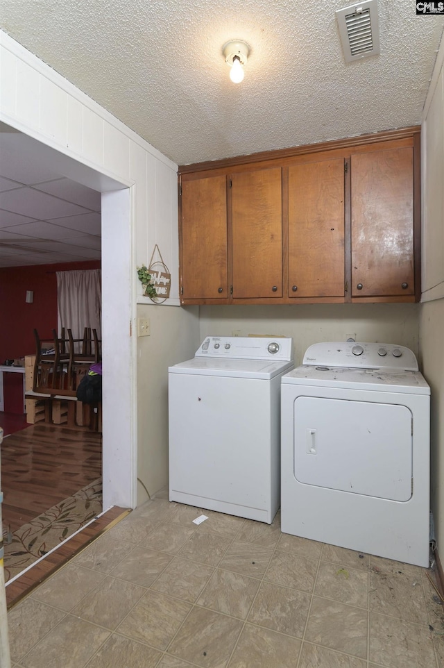 clothes washing area featuring a textured ceiling, separate washer and dryer, cabinet space, and visible vents