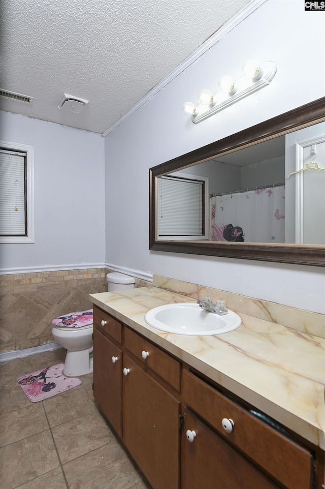 bathroom with a textured ceiling, vanity, visible vents, tile walls, and wainscoting