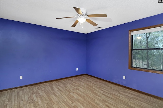 empty room with a textured ceiling, wood finished floors, a ceiling fan, visible vents, and baseboards