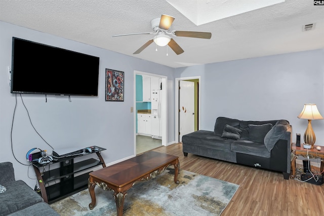 living room featuring a ceiling fan, visible vents, a textured ceiling, and wood finished floors