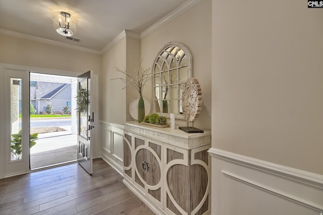 entryway featuring visible vents, a decorative wall, ornamental molding, wainscoting, and wood finished floors