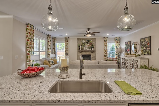 kitchen with decorative light fixtures, ornamental molding, open floor plan, a large fireplace, and a sink