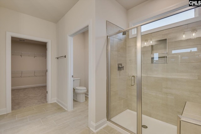 full bath featuring a spacious closet, a shower stall, toilet, and baseboards