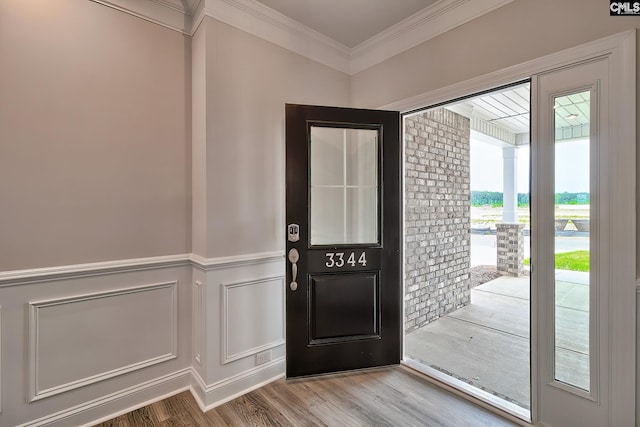 doorway to outside with a wainscoted wall, ornamental molding, a decorative wall, and wood finished floors