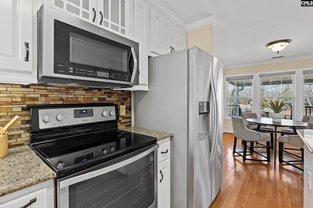 kitchen featuring decorative backsplash, ornamental molding, stainless steel appliances, light wood-style floors, and white cabinetry