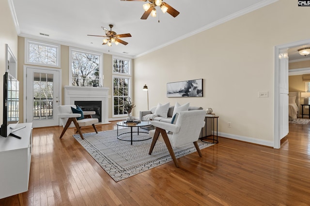 living room with hardwood / wood-style flooring, visible vents, crown molding, and a glass covered fireplace