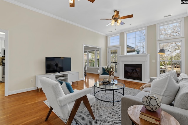 living room featuring light wood finished floors, baseboards, visible vents, and crown molding