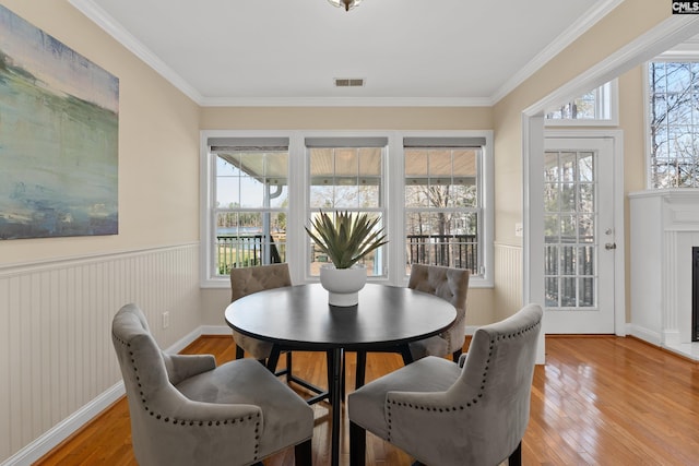 dining space with light wood finished floors, plenty of natural light, a fireplace, and a wainscoted wall