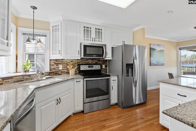 kitchen with hanging light fixtures, appliances with stainless steel finishes, ornamental molding, white cabinetry, and a sink