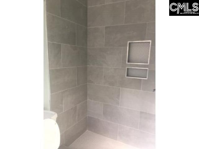 full bathroom with a tile shower and toilet