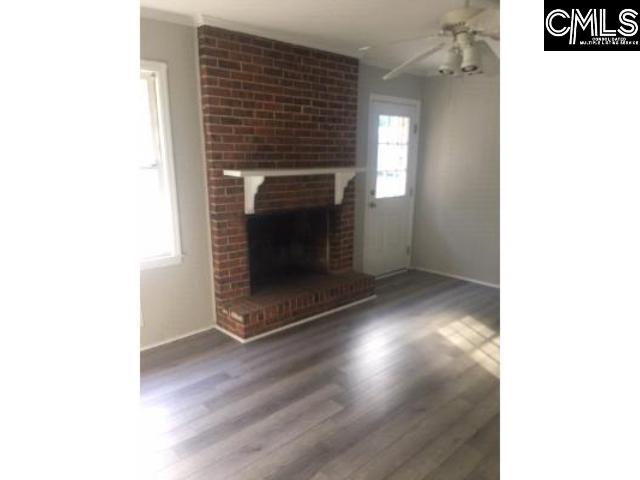 unfurnished living room featuring ceiling fan, a brick fireplace, wood finished floors, and baseboards