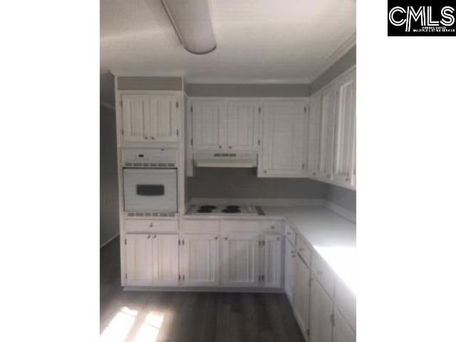 kitchen with under cabinet range hood, white appliances, dark wood-type flooring, white cabinetry, and light countertops