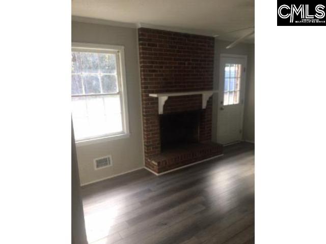 unfurnished living room featuring a brick fireplace, visible vents, and wood finished floors