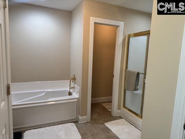 bathroom featuring a stall shower, a bath, and baseboards