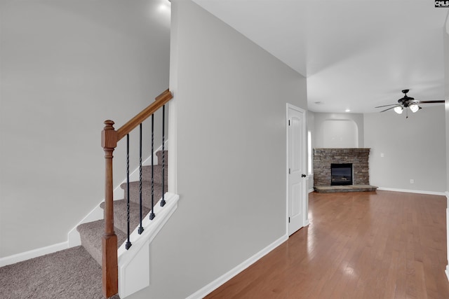 stairs with a ceiling fan, a stone fireplace, baseboards, and wood finished floors