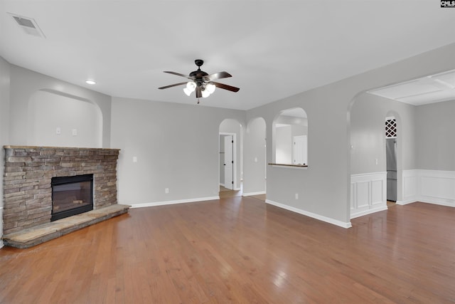 unfurnished living room featuring ceiling fan, a stone fireplace, wood finished floors, and visible vents