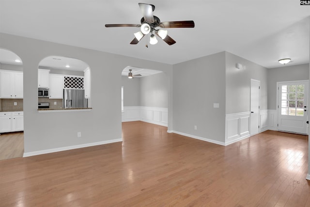 unfurnished living room featuring light wood-style floors, wainscoting, and a ceiling fan