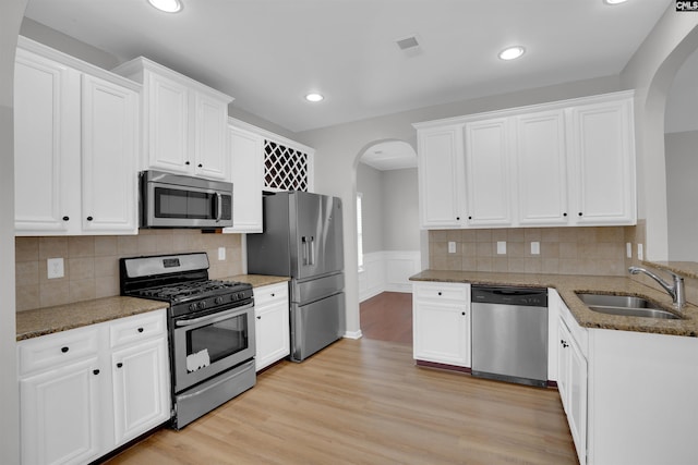 kitchen featuring arched walkways, light wood finished floors, stainless steel appliances, a sink, and light stone countertops