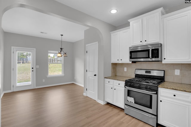 kitchen featuring arched walkways, appliances with stainless steel finishes, light wood-style flooring, and tasteful backsplash