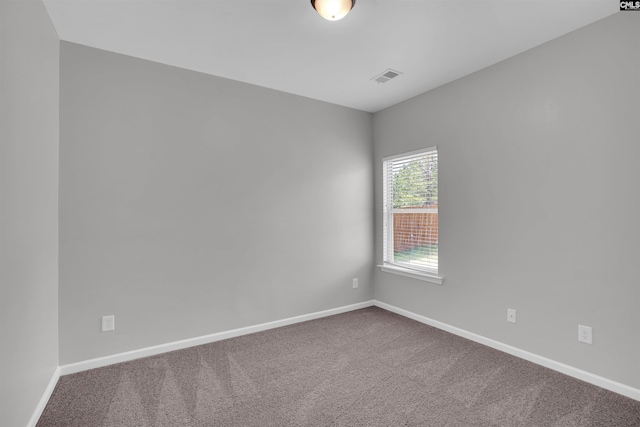 spare room featuring dark colored carpet, visible vents, and baseboards