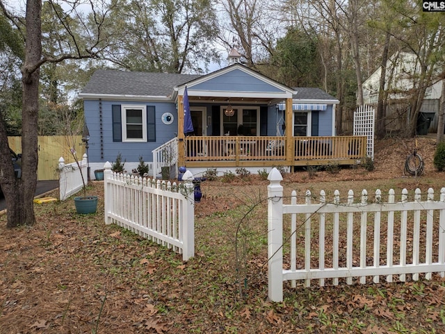 view of front facade featuring fence, covered porch, and roof with shingles