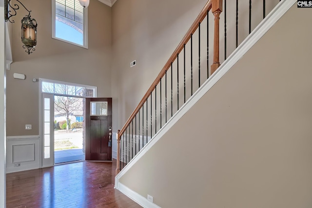 entryway with stairway, wood finished floors, visible vents, a towering ceiling, and wainscoting