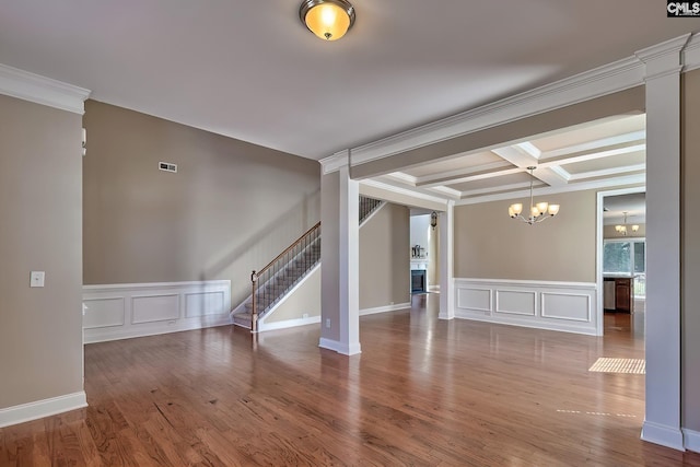 empty room featuring stairs, wood finished floors, a notable chandelier, a decorative wall, and coffered ceiling