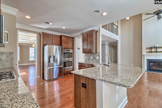 kitchen featuring tasteful backsplash, ornamental molding, light wood-style flooring, appliances with stainless steel finishes, and a sink