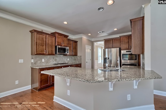 kitchen with a peninsula, appliances with stainless steel finishes, a kitchen bar, light wood-type flooring, and backsplash