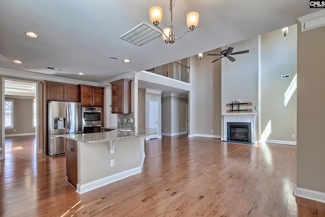 kitchen featuring light stone countertops, a breakfast bar area, ceiling fan with notable chandelier, appliances with stainless steel finishes, and wood finished floors