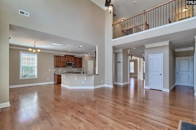 unfurnished living room with visible vents, light wood-style floors, crown molding, baseboards, and a chandelier