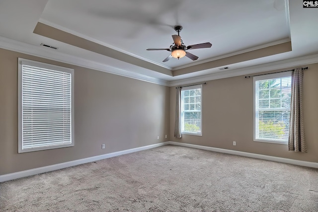 carpeted empty room featuring a raised ceiling, crown molding, and baseboards