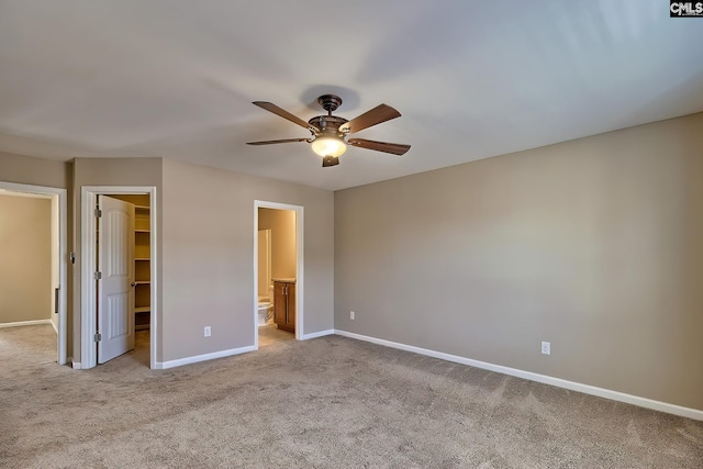 unfurnished bedroom with a spacious closet, baseboards, light carpet, a closet, and ensuite bath