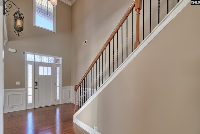 foyer entrance with visible vents, stairway, wainscoting, wood finished floors, and a decorative wall