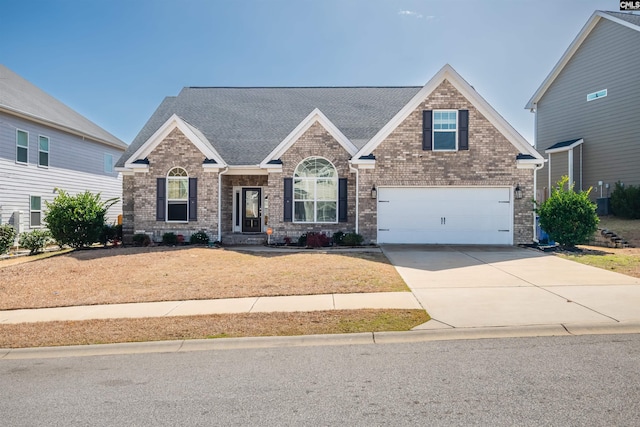 view of front of home featuring driveway, a shingled roof, a garage, and brick siding