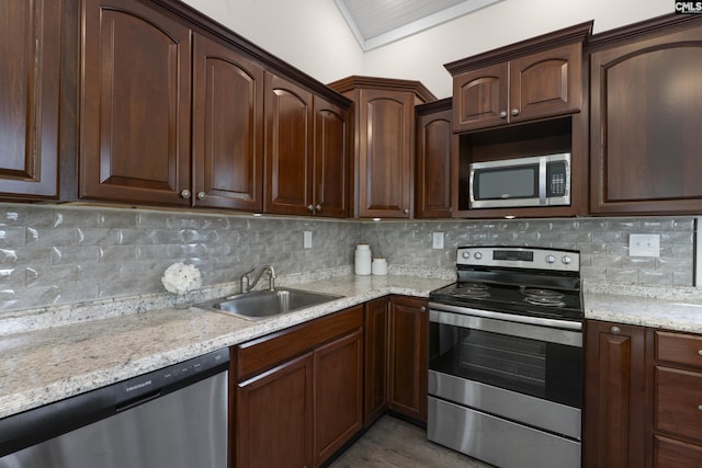 kitchen featuring decorative backsplash, light stone counters, appliances with stainless steel finishes, dark brown cabinets, and a sink