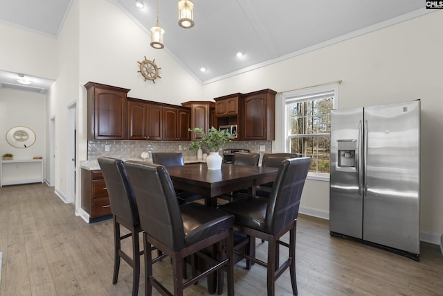 dining space with high vaulted ceiling, ornamental molding, light wood-style flooring, and baseboards