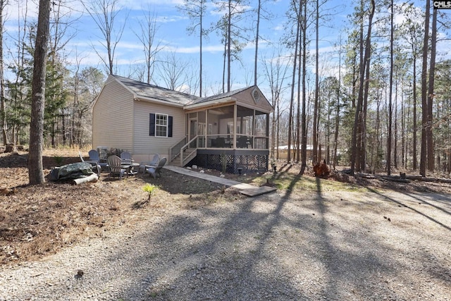 view of home's exterior with gravel driveway, a sunroom, and stairs