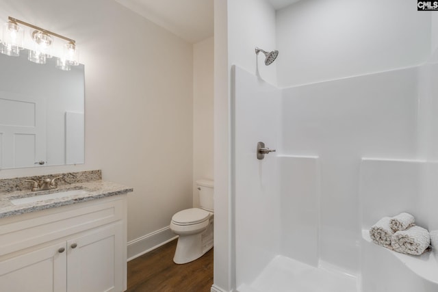 bathroom with toilet, vanity, wood finished floors, baseboards, and walk in shower