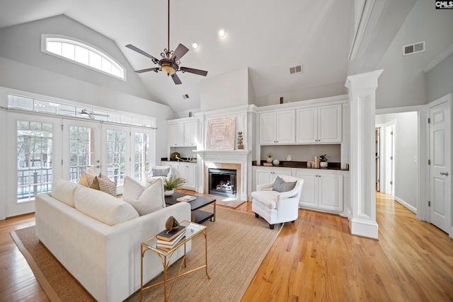 living area featuring ornate columns, visible vents, a fireplace with raised hearth, and light wood-style floors