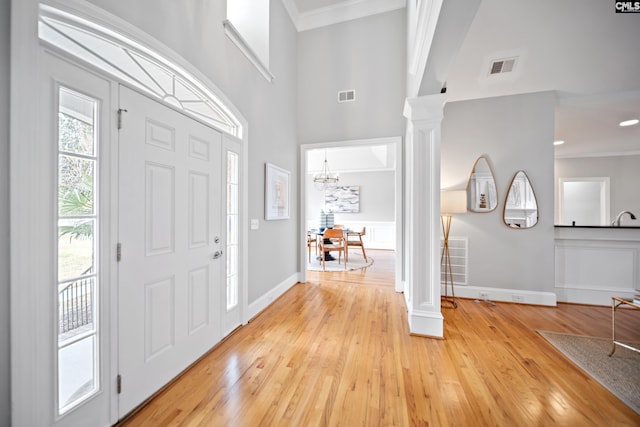 entryway with light wood-type flooring, visible vents, decorative columns, and a towering ceiling