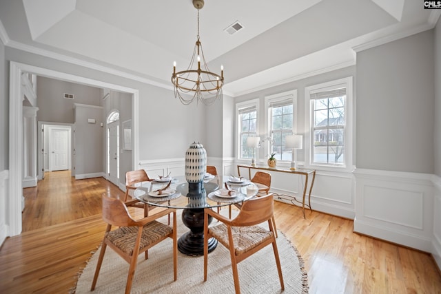 dining area featuring a tray ceiling, light wood-type flooring, visible vents, and a notable chandelier