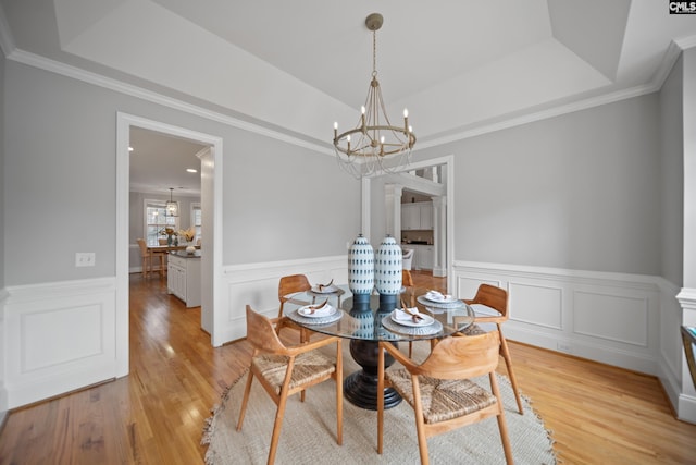 dining area with light wood-style floors, a tray ceiling, crown molding, and an inviting chandelier