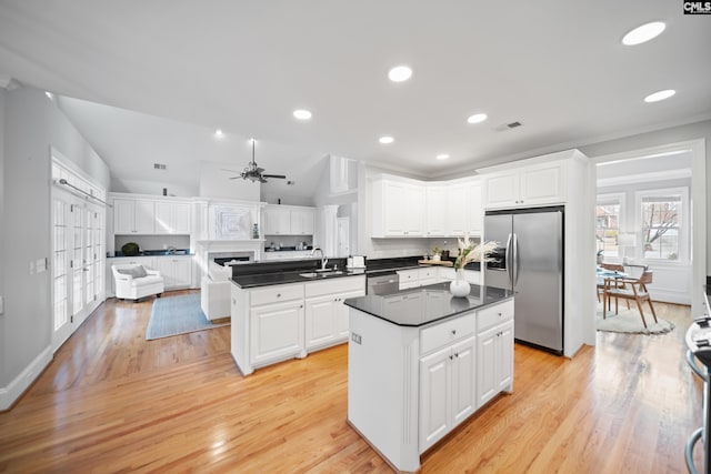 kitchen with dark countertops, a kitchen island, stainless steel appliances, white cabinetry, and a sink